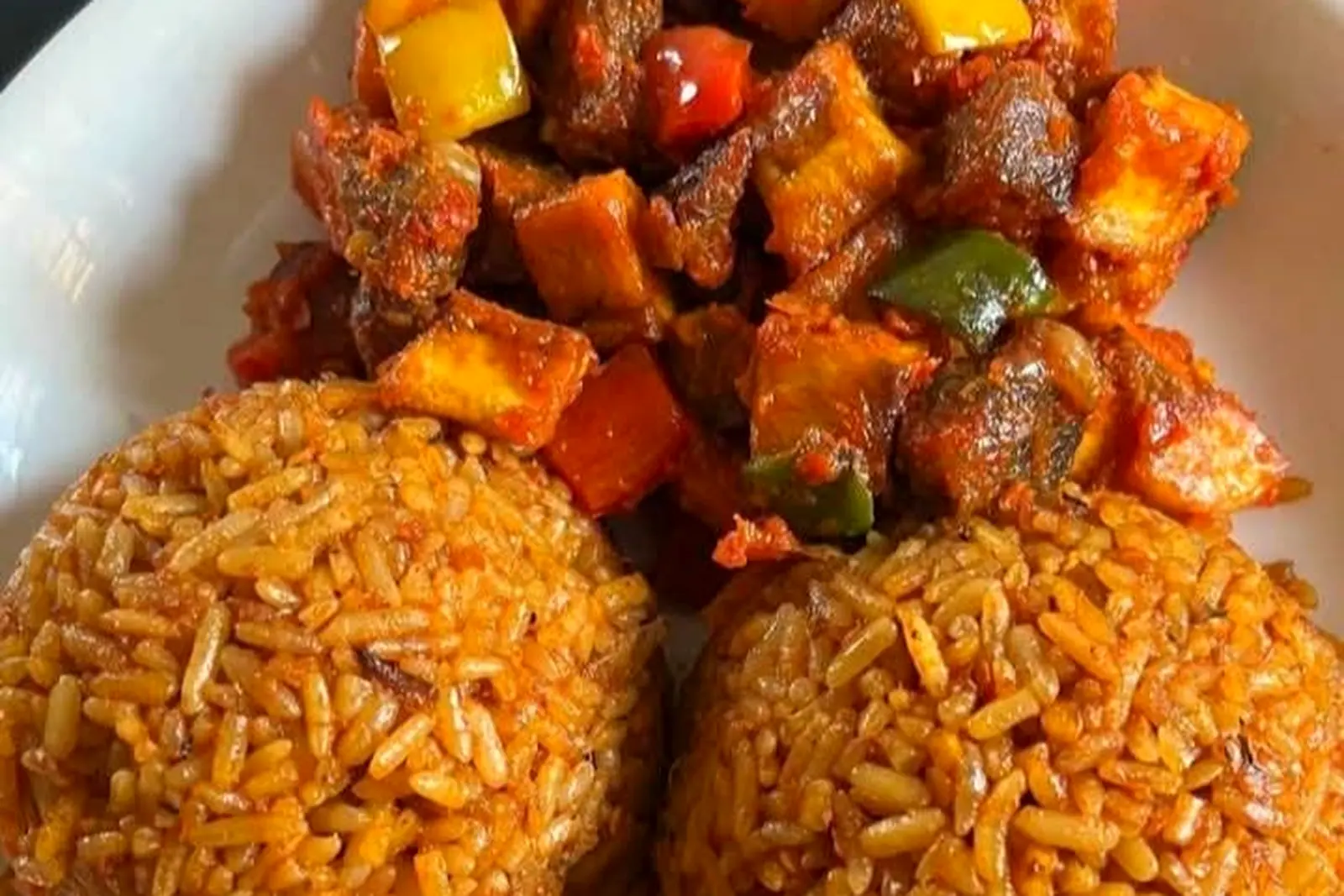 Two portions of red-orange jollof rice with stewed mutton and mixed peppers